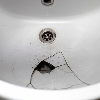 Cracked ceramic bathroom sink with visible damage.